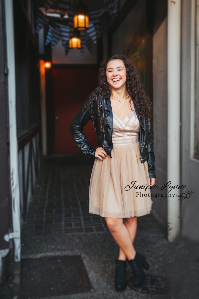 High school senior girl in rose gold homecoming dress and leather bomber jacket in downtown Poulsbo Washington what to wear with Juniper Lynne Photography in Gig Harbor