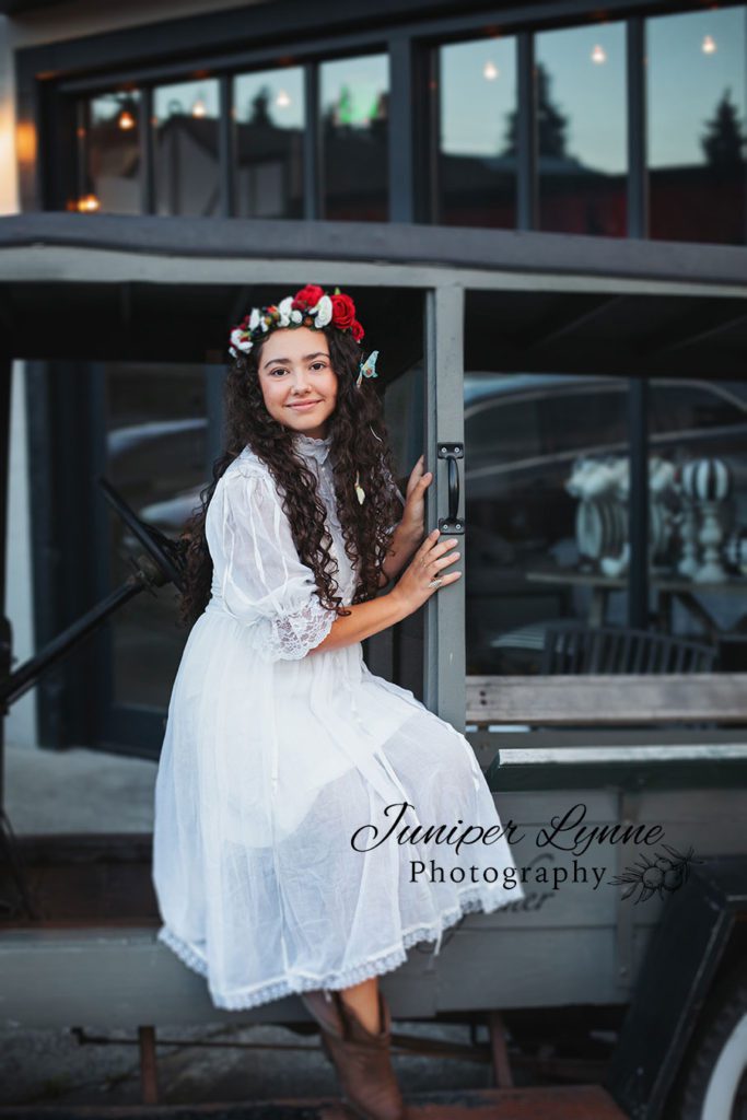 High school senior girl in red and white flower crown downtown Poulsbo Washington nordic look on old antique car what to wear boho with Juniper Lynne Photography of Gig Harbor