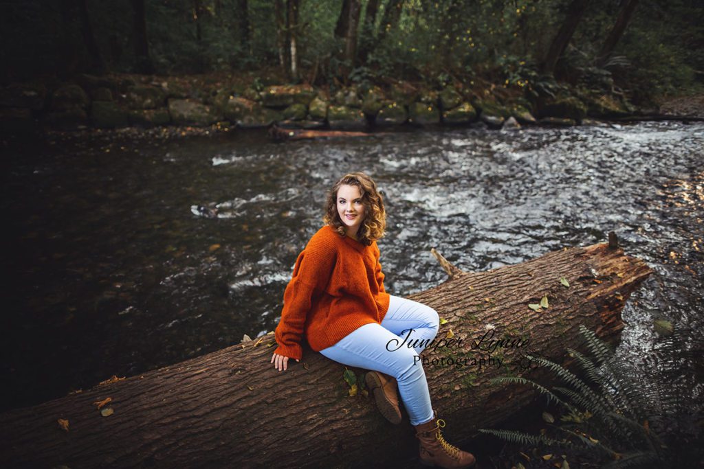 high school senior girl in cozy sweater on log on creek at Kobayashi park in Tacoma, University Place by Juniper Lynne Photography.