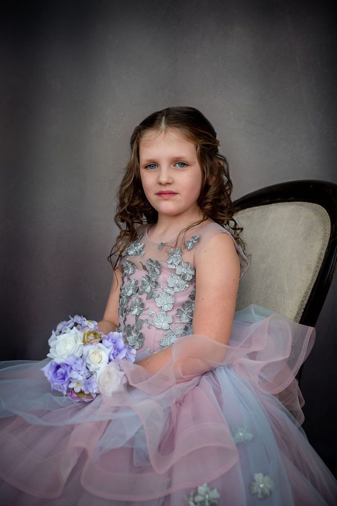 little girl siting in chair in studio portrait wearing ball gown