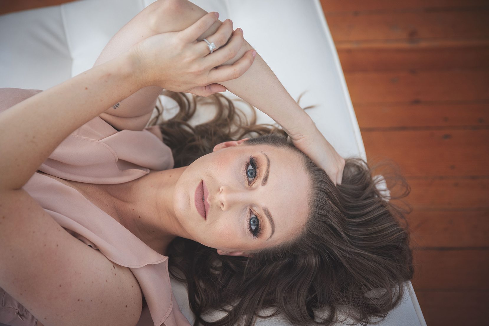 beautiful women laying down on white couch wearing pink dress with hand in hair luxury portrait experience with juniper lynne photography Tacoma washington