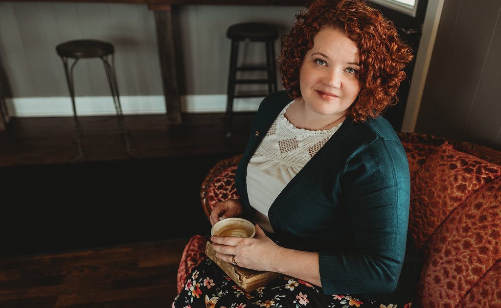 woman with red curly hair holding coffee and smiling at the camera.