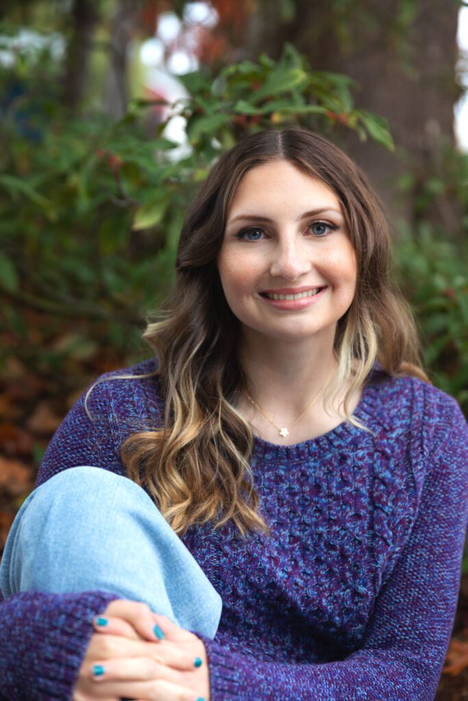 High school senior posing for photo. She is wearing purple sweater and jeans. 