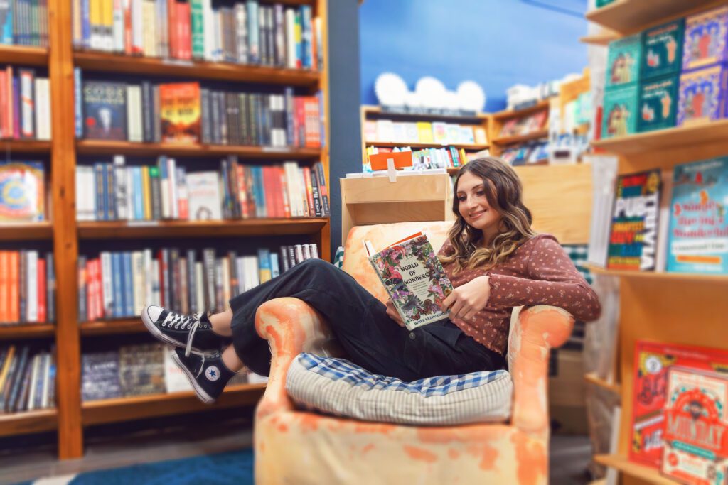 high school senior girl reading a book in a big chair in a book shop in downtown Poulsbo Washington by Juniper Lynne Photography. Fall colors are used.